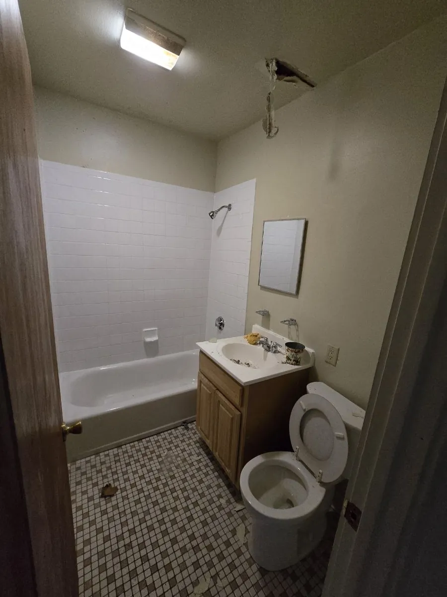 Apartment bathroom before the renovation: old wall tile, single-handle shower valve, dated vanity and an open hole in the ceiling