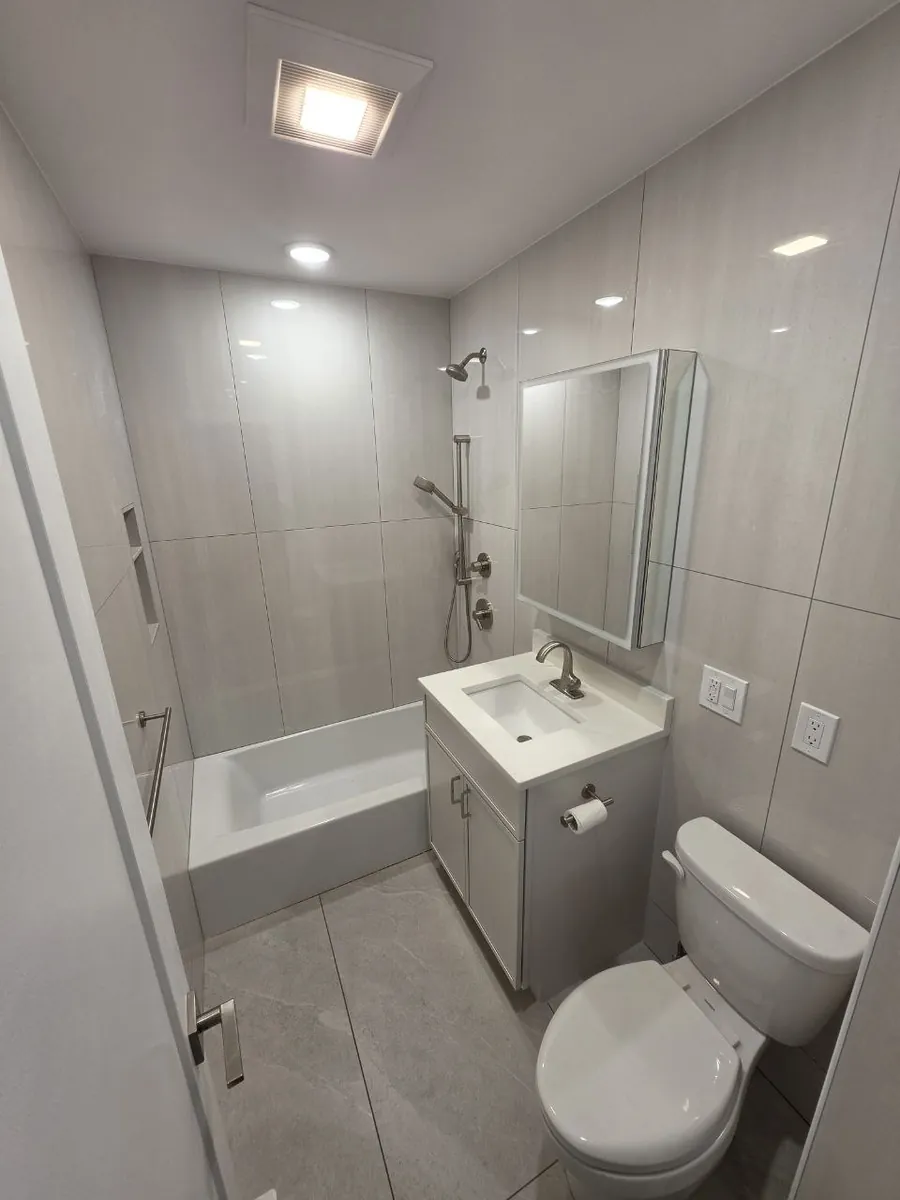 The same bathroom after the renovation: new tub and shower valve, handheld shower slide bar, new vanity and toilet