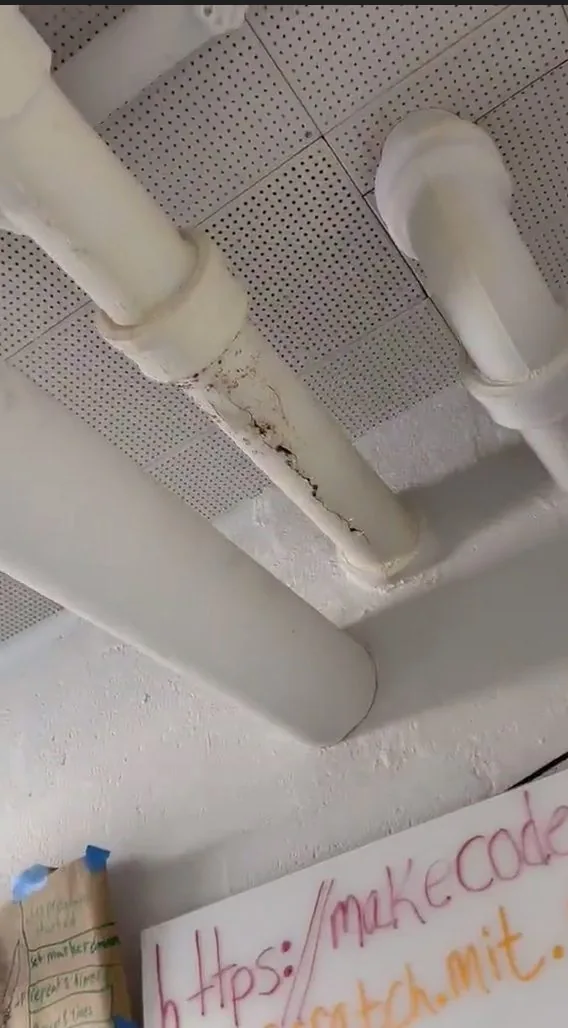 Cracked cast-iron sewer pipe leaking at a school ceiling