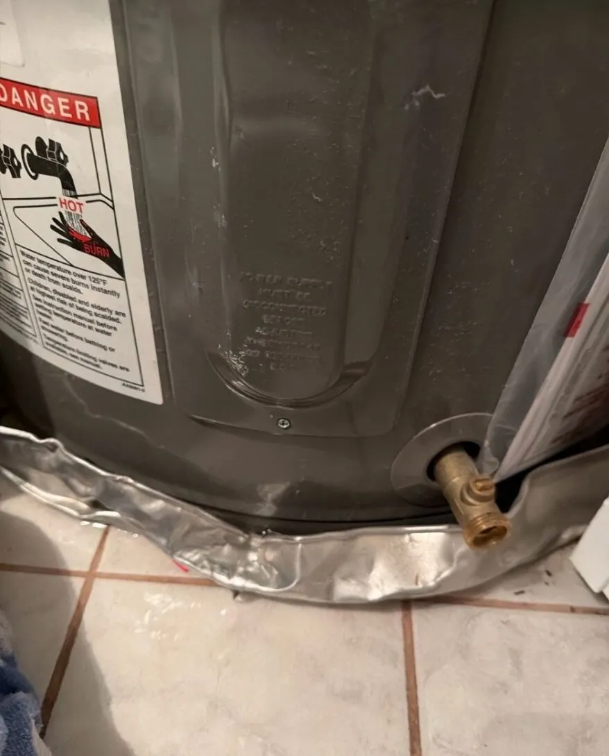 Rusted-through drain pan under the old water heater with holes and corrosion