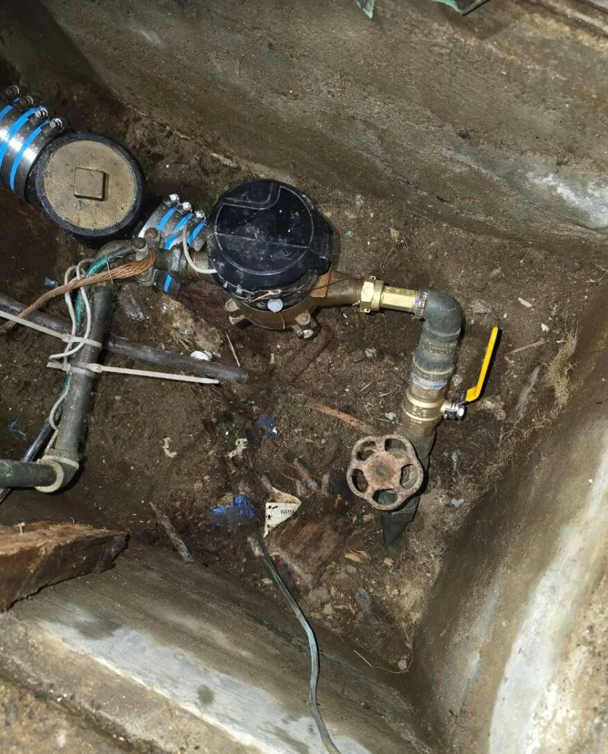 Close-up of the corroded gate valve and water meter connection inside the pit