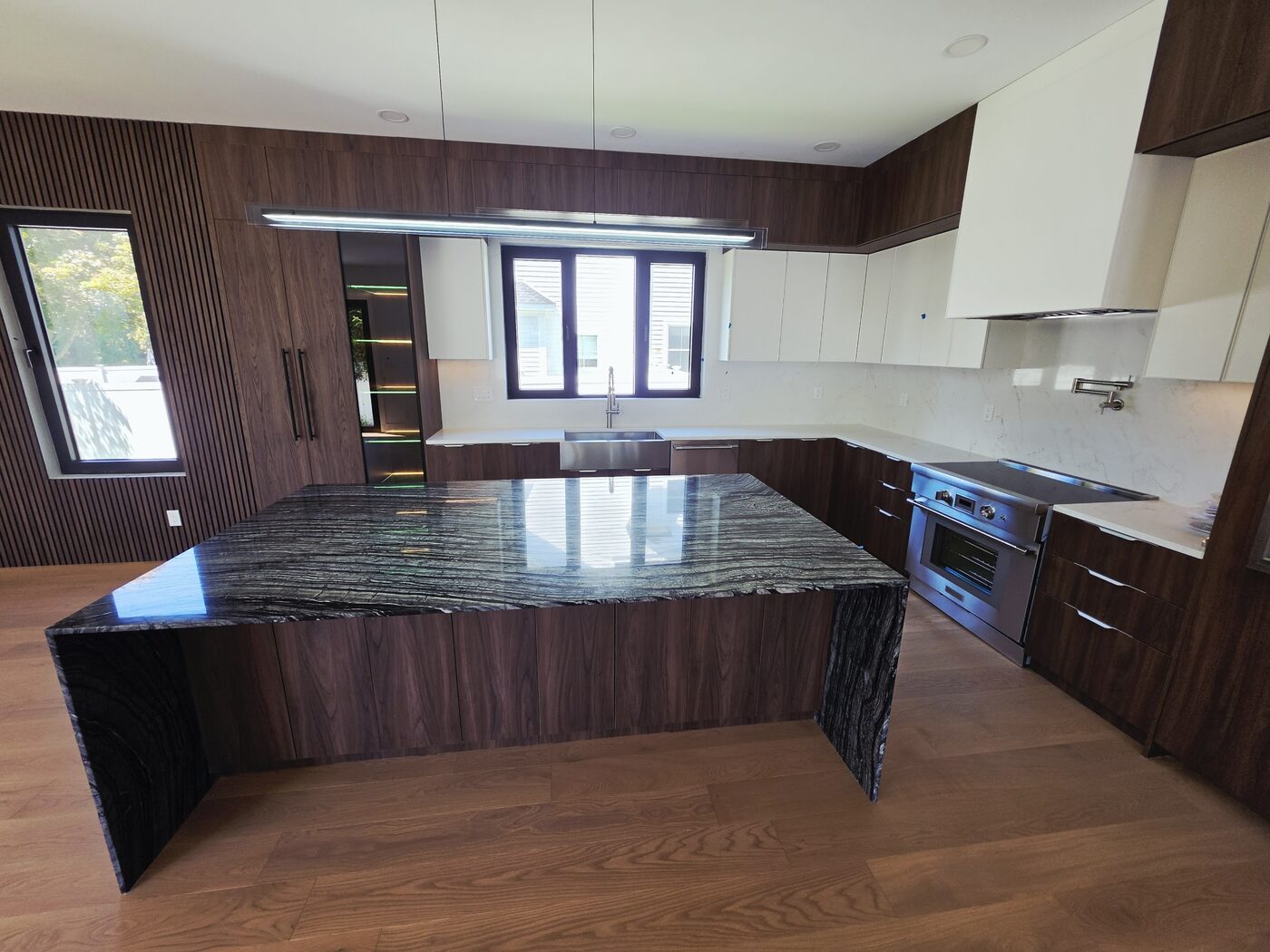 Custom kitchen with walnut cabinetry and a black marble waterfall island, plumbed by IS Plumbing