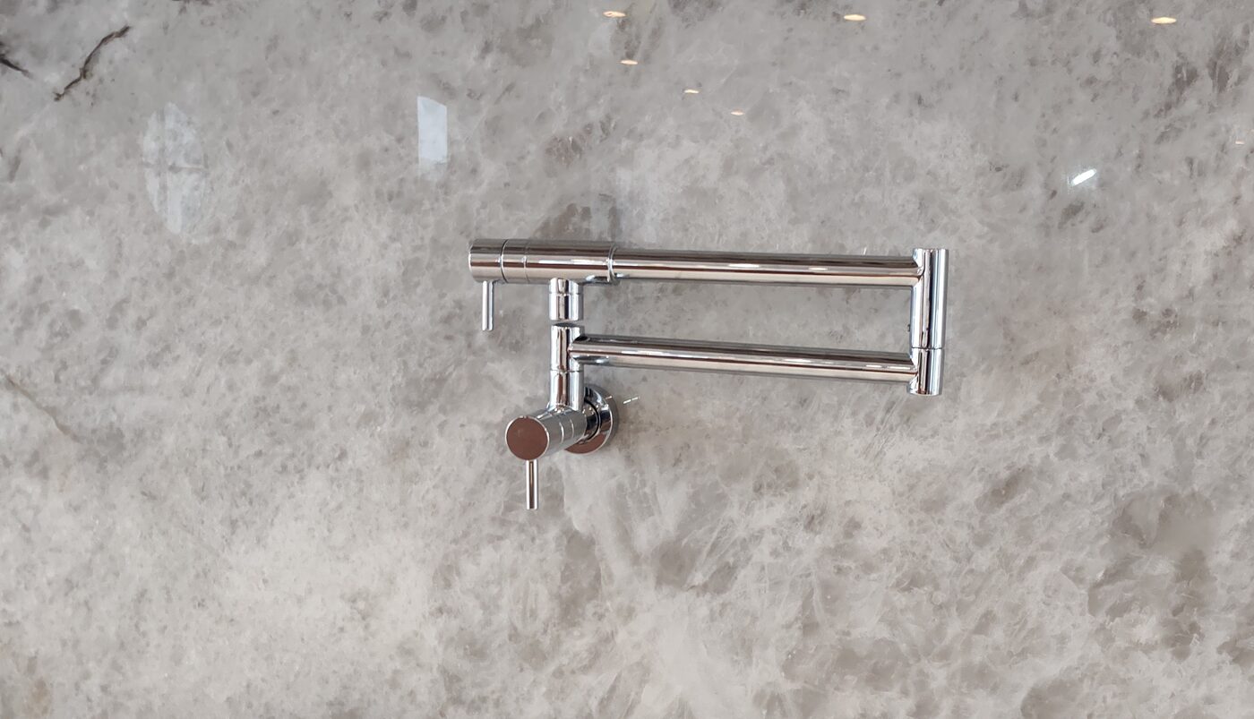 Wall-mounted folding pot filler faucet installed over a stone backsplash
