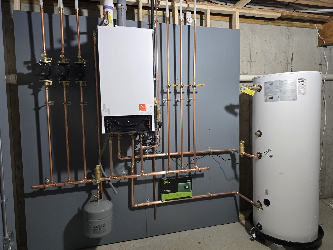 Tankless water heater paired with a large storage tank and copper piping