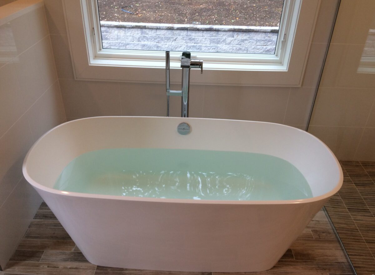 Freestanding soaking tub with a chrome floor-mounted tub filler beneath a frosted window